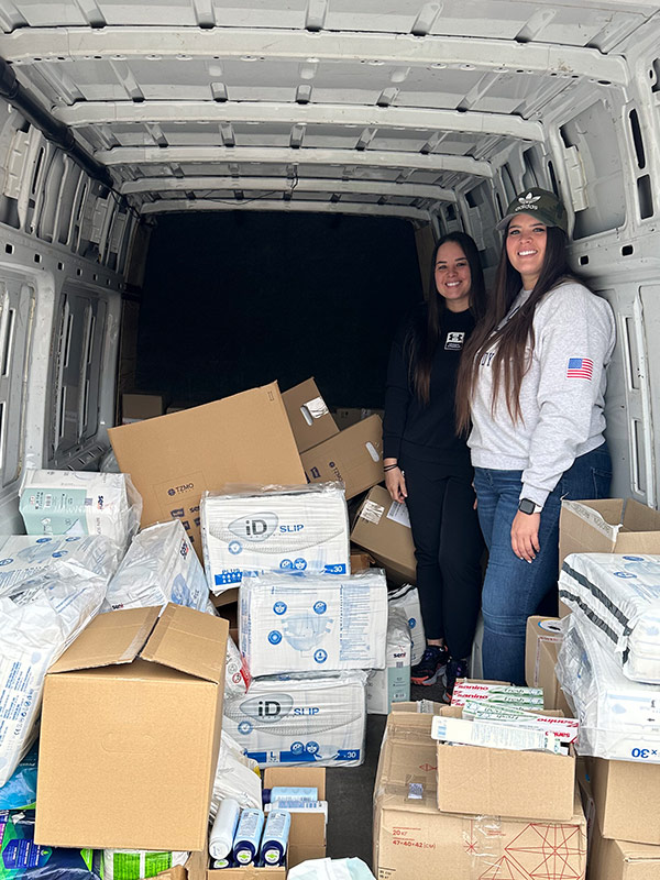 Redwood Global founders Samantha and Hope standing in a vehicle filled with home supplies.