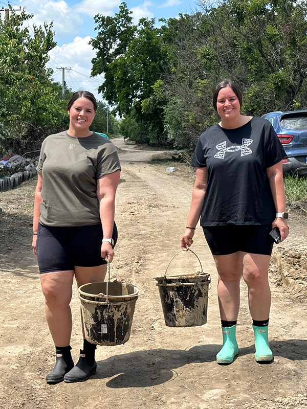 Two women carrying buckets down a dirt road.